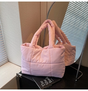 Detailed view of the pink quilted down tote bag with a soft puffy texture on reflective wood