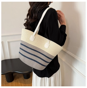Detail of a large straw tote bag with blue stripes and white leather straps on a model