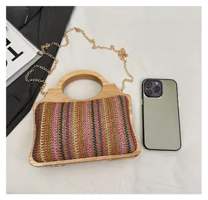 Detalle de bolso de paja tejido colorido con asa de bambú y cadena dorada junto a un móvil
