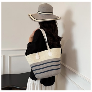 Back view of a model wearing a large striped woven tote bag and matching straw sun hat