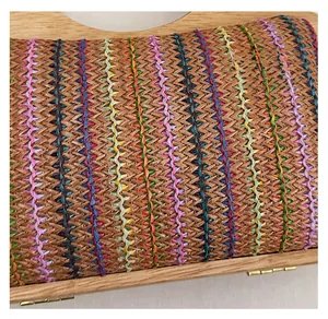 Detalle del bolso de paja trenzada con costuras coloridas y asa de madera natural