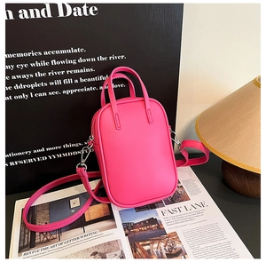 Macro detail of a hot pink mini crossbody bag with leather handles on an open magazine