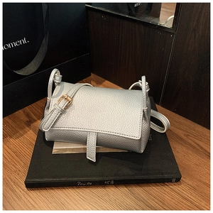 Close-up of a silver lychee-textured crossbody bag on books with a metallic buckle detail