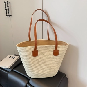 Detail of hand-woven straw tote bag featuring brown leather straps and spacious interior