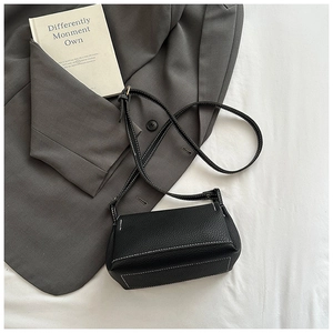 Detail of black pebbled leather crossbody bag with contrasting white stitching accents