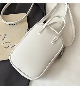 Overhead view of minimalist white square crossbody bag with top handles on bicolor background