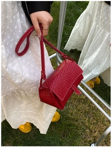 Détail de la texture tressée rouge sur un sac à rabat avec des coutures blanches fines