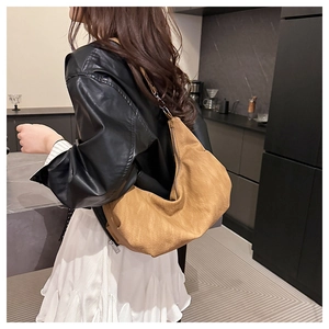 Detailed view of warm brown pleated leather shoulder bag worn by model in modern kitchen
