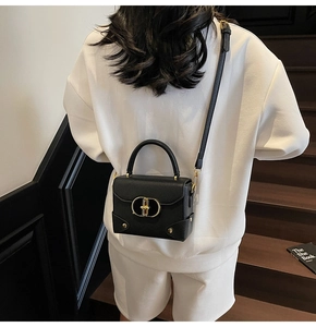 Detail view of black lychee grain leather crossbody bag with golden oval metal lock
