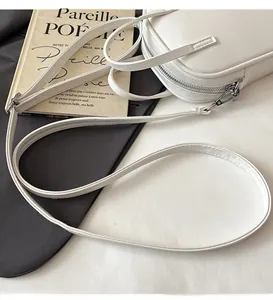Detail view of smooth silver zipper and leather strap on a minimalist white crossbody bag