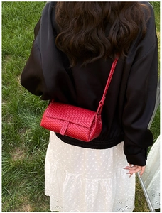 Vue extérieure d'un sac bandoulière rouge vif à texture tissée porté par un modèle