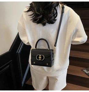 Detail of black pebbled leather handbag with gold metal clasp on a stylish shoulder strap