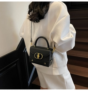 Detail of black pebbled leather handbag featuring gold round buckle and metal handle