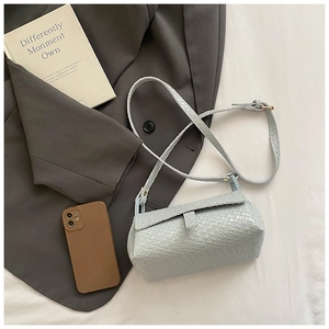Détail de la texture tressée bleu clair et du fermoir à rabat d'un sac à bandoulière