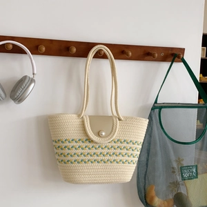 Beige gewebte Strohtasche mit Wellenmuster und großer Perle an einem Wandhaken