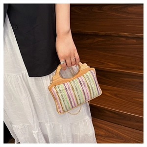 Detalle de bolso de paja tejida de colores con asa de madera tallada y cadena dorada