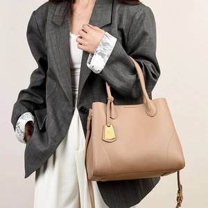 Close-up of beige lychee grain leather handbag with gold metal logo and dual handle straps