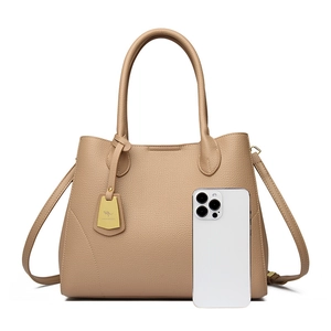 Detail view of khaki leather tote bag showing size comparison with a white iPhone