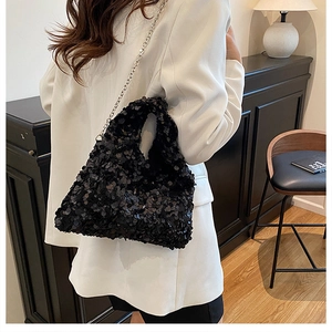 Detail of a chic black sequined hobo bag with silver chain strap on a white blazer
