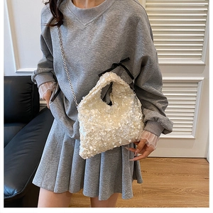 Detail of white sequin dumpling bag with metallic chain strap worn by a model