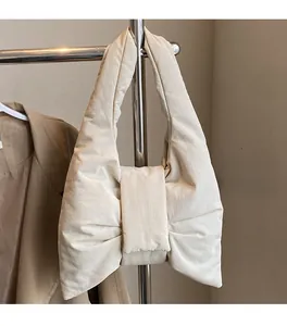 Detail view of cream oversized bow handbag hanging on metal rack with soft texture