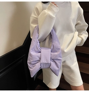 Model showcasing a large purple bow-shaped puffy handbag made of textured nylon material