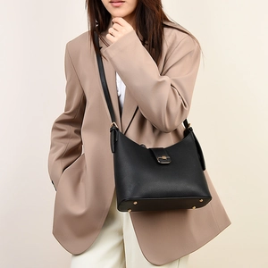 Close-up of black lychee grain leather bucket bag with gold metal clasp on a model