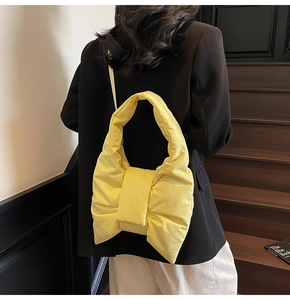 Bright yellow bow-shaped padded shoulder bag shown on model with quilted texture detail