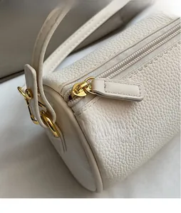 Detail of white lychee leather texture and glossy gold zipper hardware on cylindrical bag