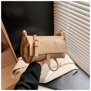 Sac bandoulière kaki à texture tissée tenu à la main dans un cadre minimaliste chic
