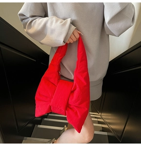 Detail of red bow-shaped tote bag with soft padded texture carried by a model on stairs