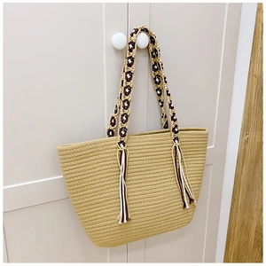 Detail of summer straw tote bag featuring ethnic braided strap and tassel accents