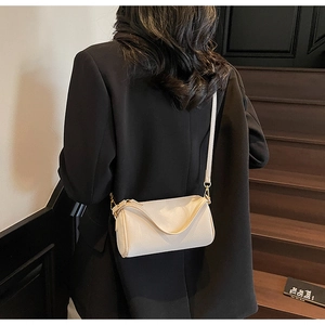 Model wearing a minimalist cream-white cylinder crossbody bag on modern stairs