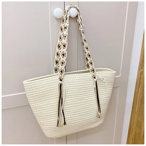 Detail of hand-woven beige straw tote bag with braided shoulder strap and brown tassels
