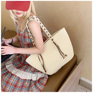 Detail of cream straw tote bag featuring decorative long tassels and ethnic jacquard strap