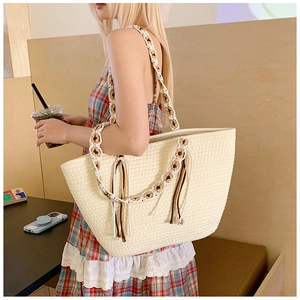 Detail of bohemian straw tote bag featuring woven flower handles and chic tassels