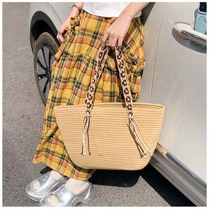 Close-up of woven straw tote bag featuring contrast tassel handles and bohemian texture