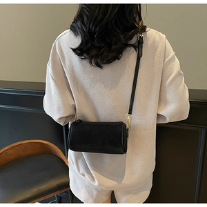 Detailed back view of a black cylinder crossbody bag featuring gold hardware on a model