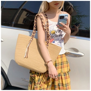 Detail of a beige straw tote bag with contrast woven straps and fringe tassels
