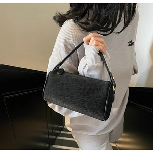 Detail of black lychee grain cylinder bag with gold hardware on a shoulder strap