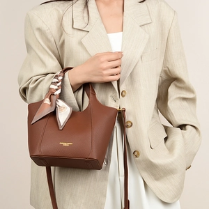 Detail of a brown leather tote with a silk scarf wrapped handle and golden logo