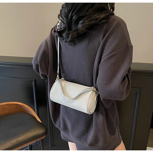 Detail of light grey cylinder leather bag with litchi texture on a brown waffle sweater