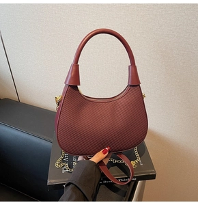 Close-up of wine red crescent bag with textured weave, gold zipper and chain strap