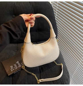 Detail of cream hobo bag showing woven texture, gold chain strap, and curved handle