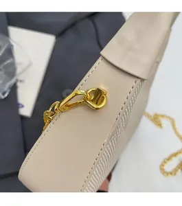 Detail of high-gloss gold chain link and lobster clasp on off-white woven shoulder bag