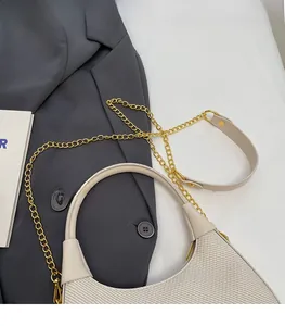 Detail of cream half-moon bag featuring textured fabric and gold chain on grey blazer