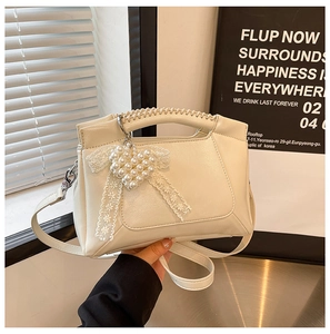 Detail of cream white handbag featuring a pearl heart charm and lace bow decoration