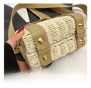 Close-up of woven straw handbag featuring khaki canvas straps and gold stud hardware details