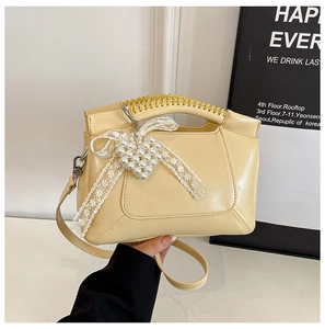 Detail of cream yellow leather handbag featuring braided handle and pearl lace bow charm