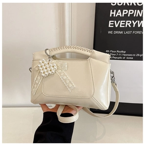 Detail of cream white bag with woven handle, pearl heart charm and metal buckles
